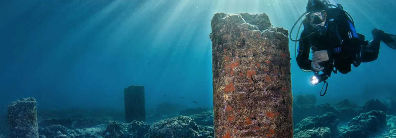 Subacqueo con la torcia accanto a una colonna romana sommersa nel parco di Baia
